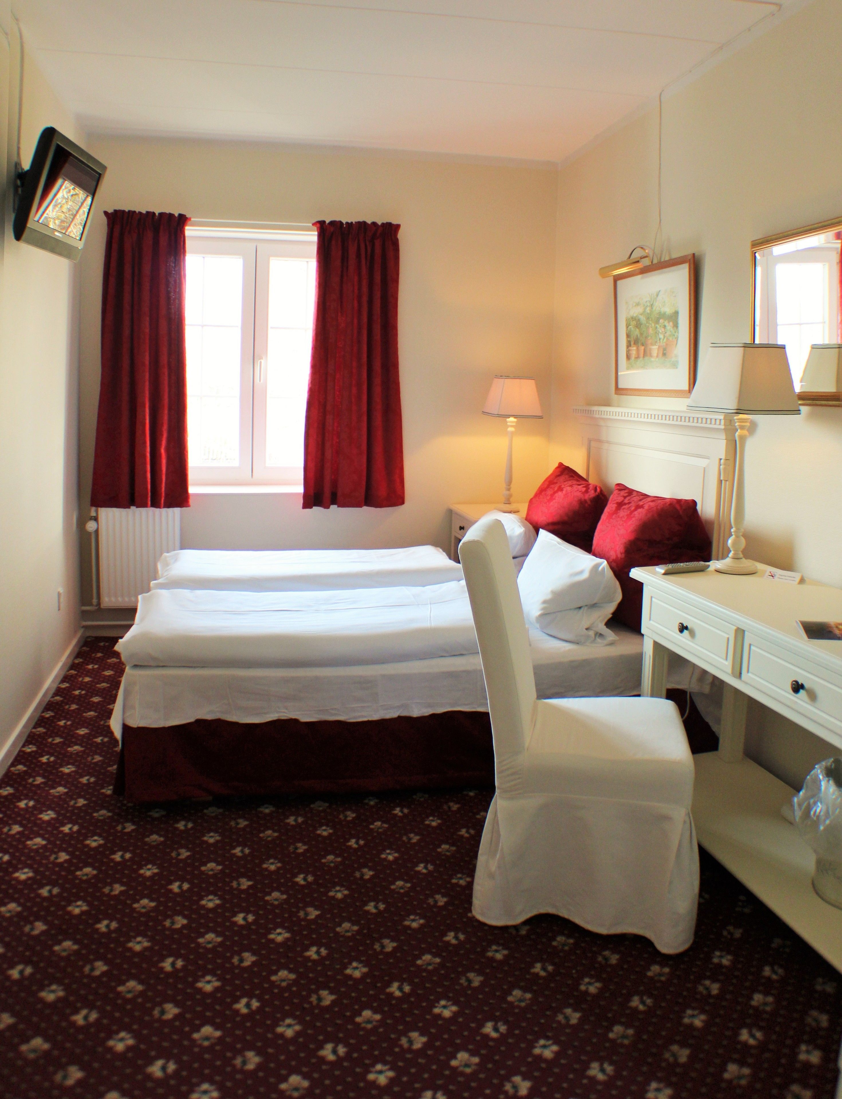 Une chambre d’hôtel avec deux lits, un bureau, une chaise, une lampe et une fenêtre avec des rideaux.