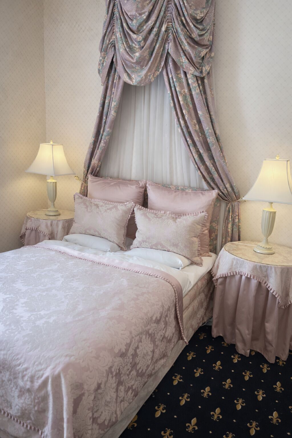 Un lit à baldaquin, deux tables de chevet avec des lampes et une moquette à motifs.