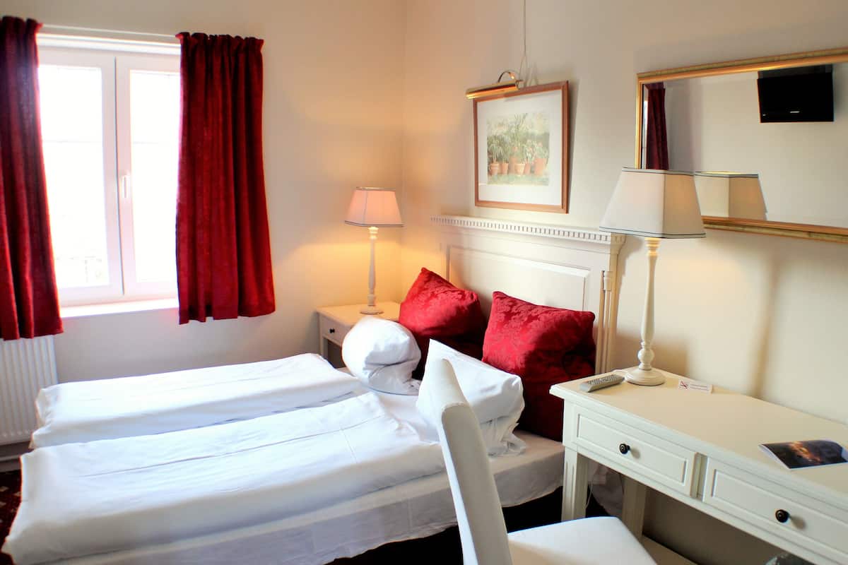 A hotel room with two beds, a desk, a chair, a lamp, a mirror, and a window with curtains.