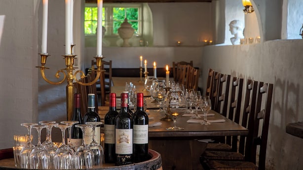 Una mesa de comedor dispuesta con botellas de vino, copas, velas y decoración clásica.