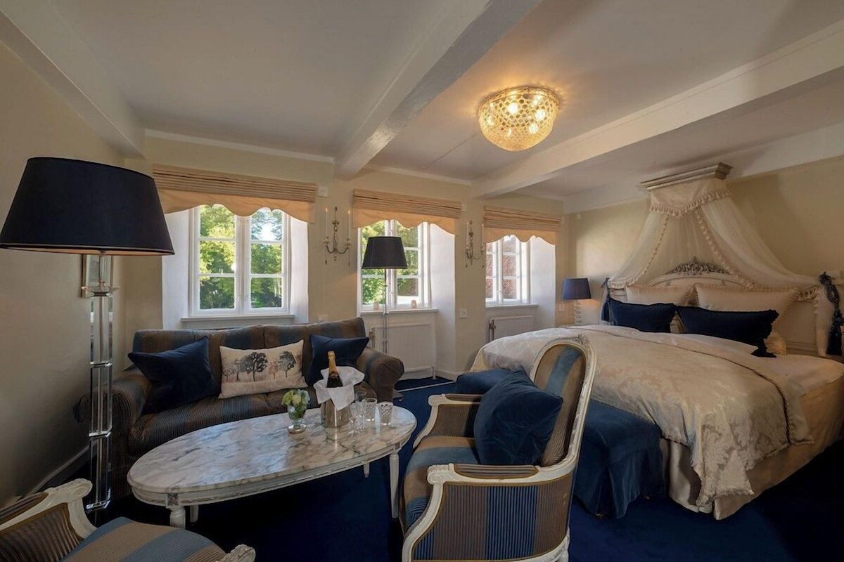 A bedroom with a canopy bed, a round table, a sofa, and a lamp.