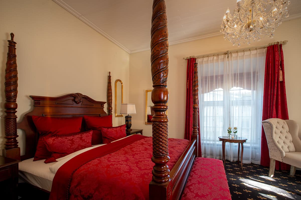 A four-poster bed with red linens, a chandelier, and a red and white striped window.