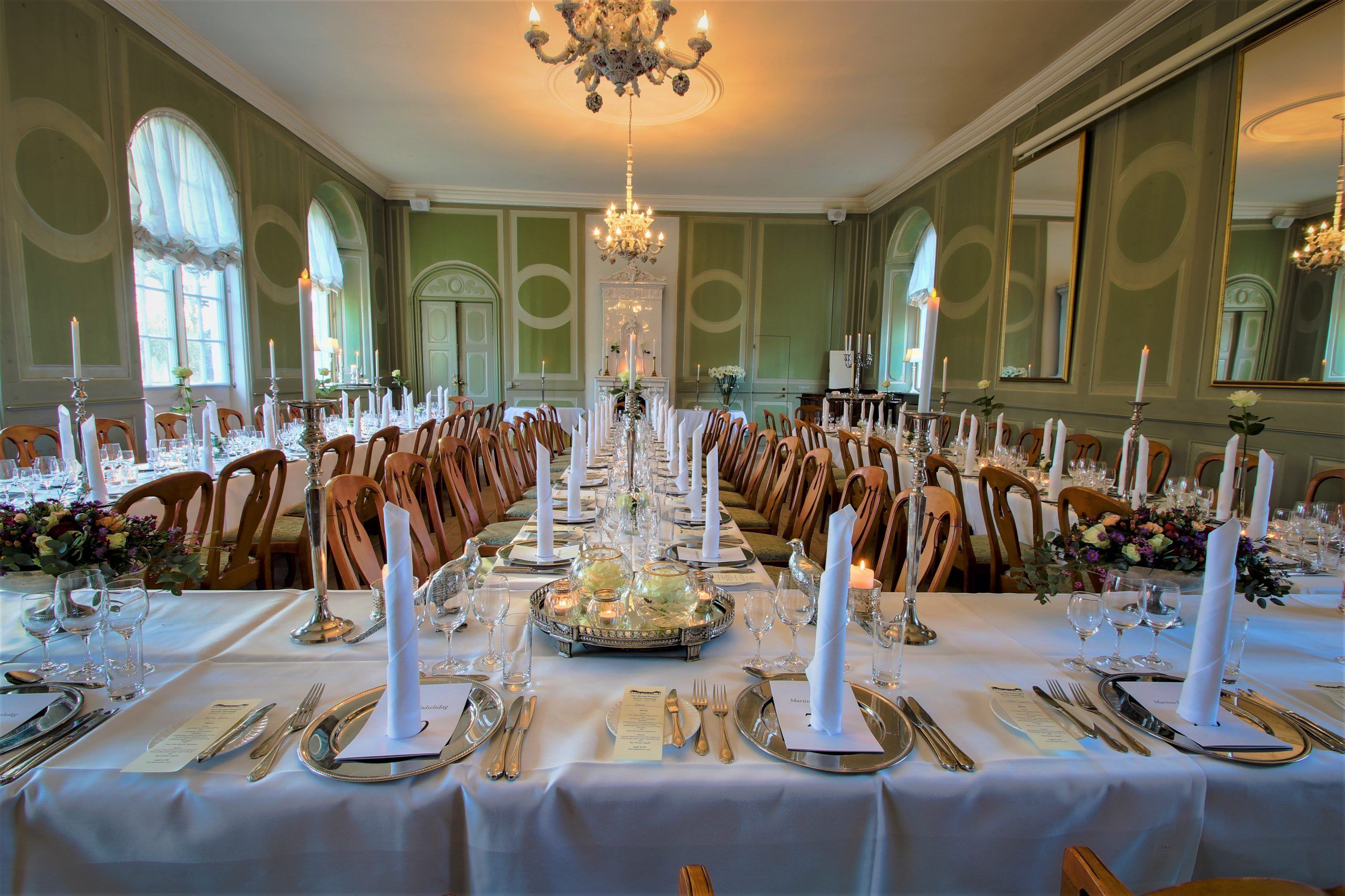 Comedor formal con mesas largas, velas y elegantes puestas de mesa.