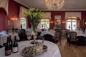 A formal dining room with tables set for service, a chandelier, and a large window.