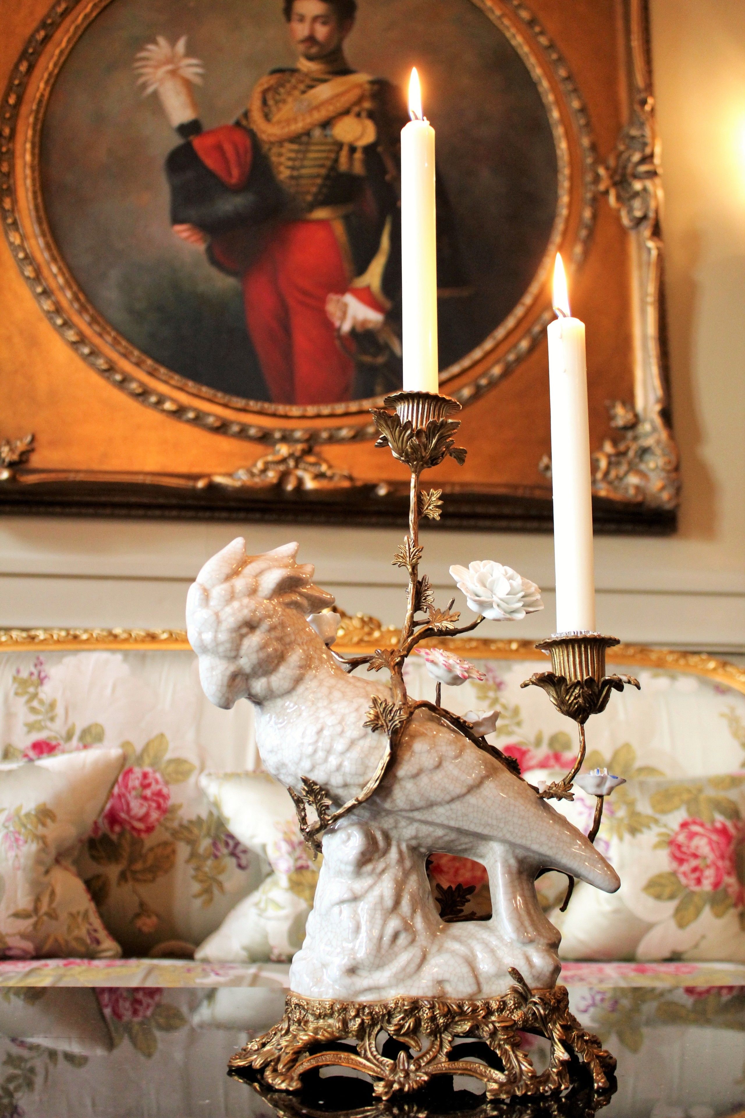 Un chandelier décoratif avec deux bougies allumées, un portrait encadré et un canapé à motifs floraux.