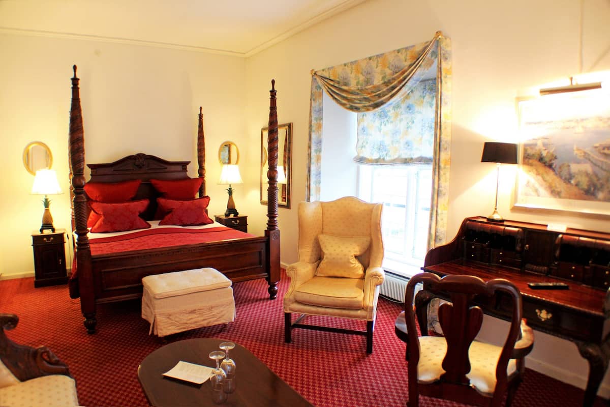 A bedroom with a four-poster bed, a sitting chair, a desk, and a small table.