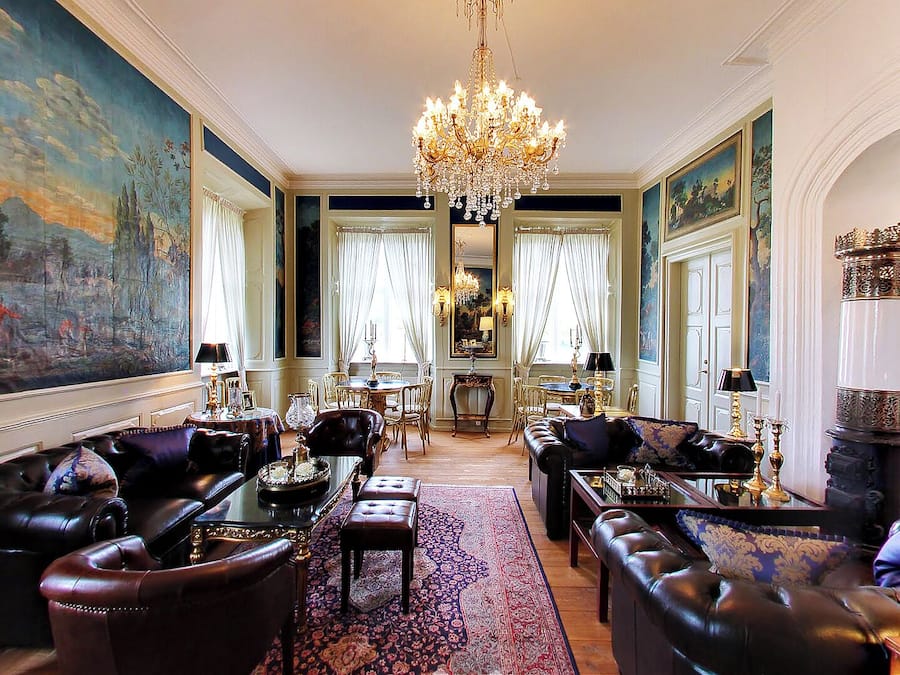 Une chambre luxueuse, dotée de canapés en cuir, d’un lustre et de tableaux classiques.