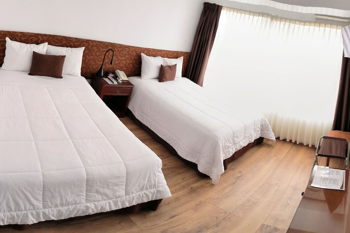 A hotel room with two beds, a wooden floor, a desk with a chair, and a framed picture on the wall.
