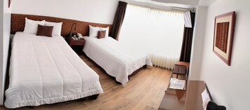 A hotel room with two beds, a wooden floor, a desk with a chair, and a framed picture on the wall.
