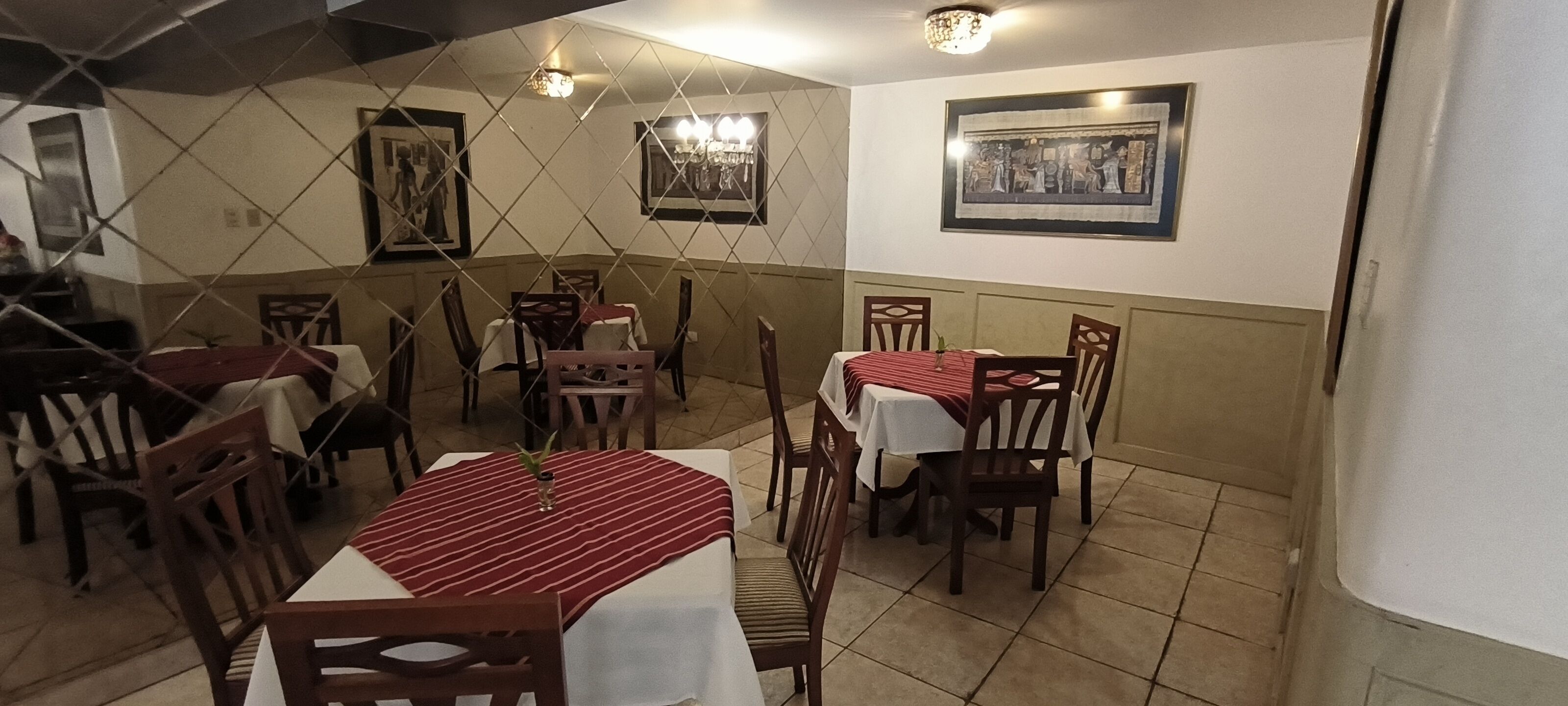 A dining area with tables and chairs, framed pictures on the walls, and a tiled floor.