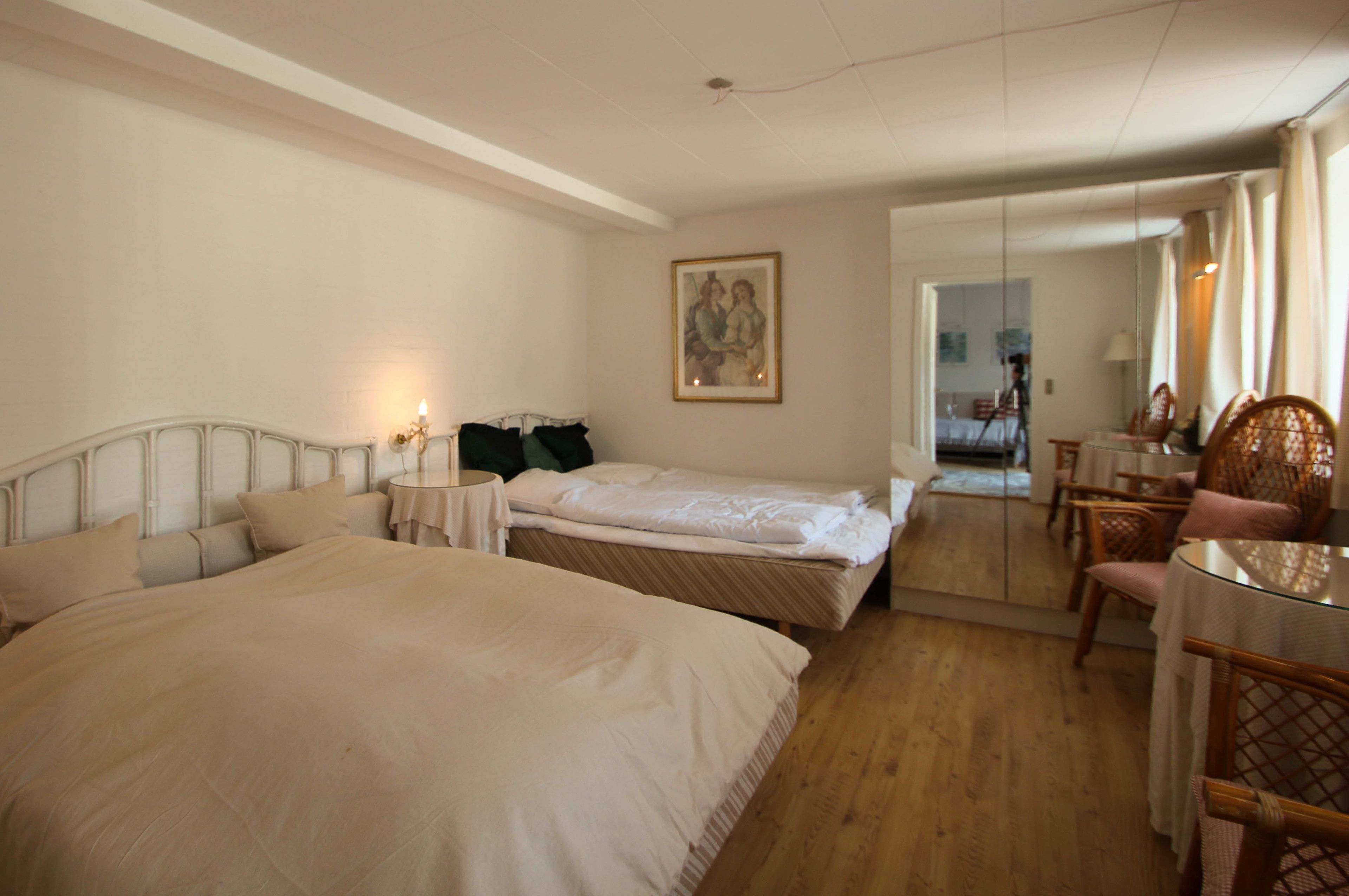 Ein Hotelzimmer mit zwei Betten, einem Esstisch mit Stühlen, einem Spiegel und einem Bild an der Wand.
