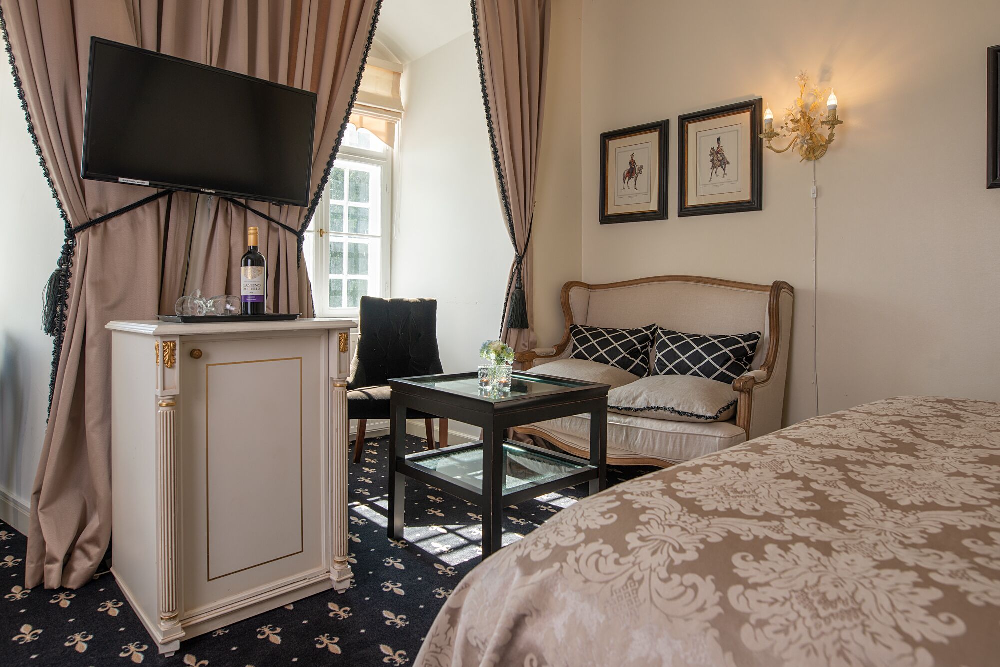 Ein Hotelzimmer mit Bett, Wandfernseher, einem kleinen Tisch mit Vase und einem Vorhangfenster.