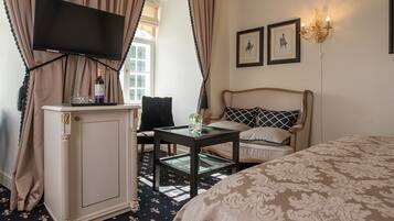 Ein Hotelzimmer mit Bett, Wandfernseher, einem kleinen Tisch mit Vase und einem Vorhangfenster.