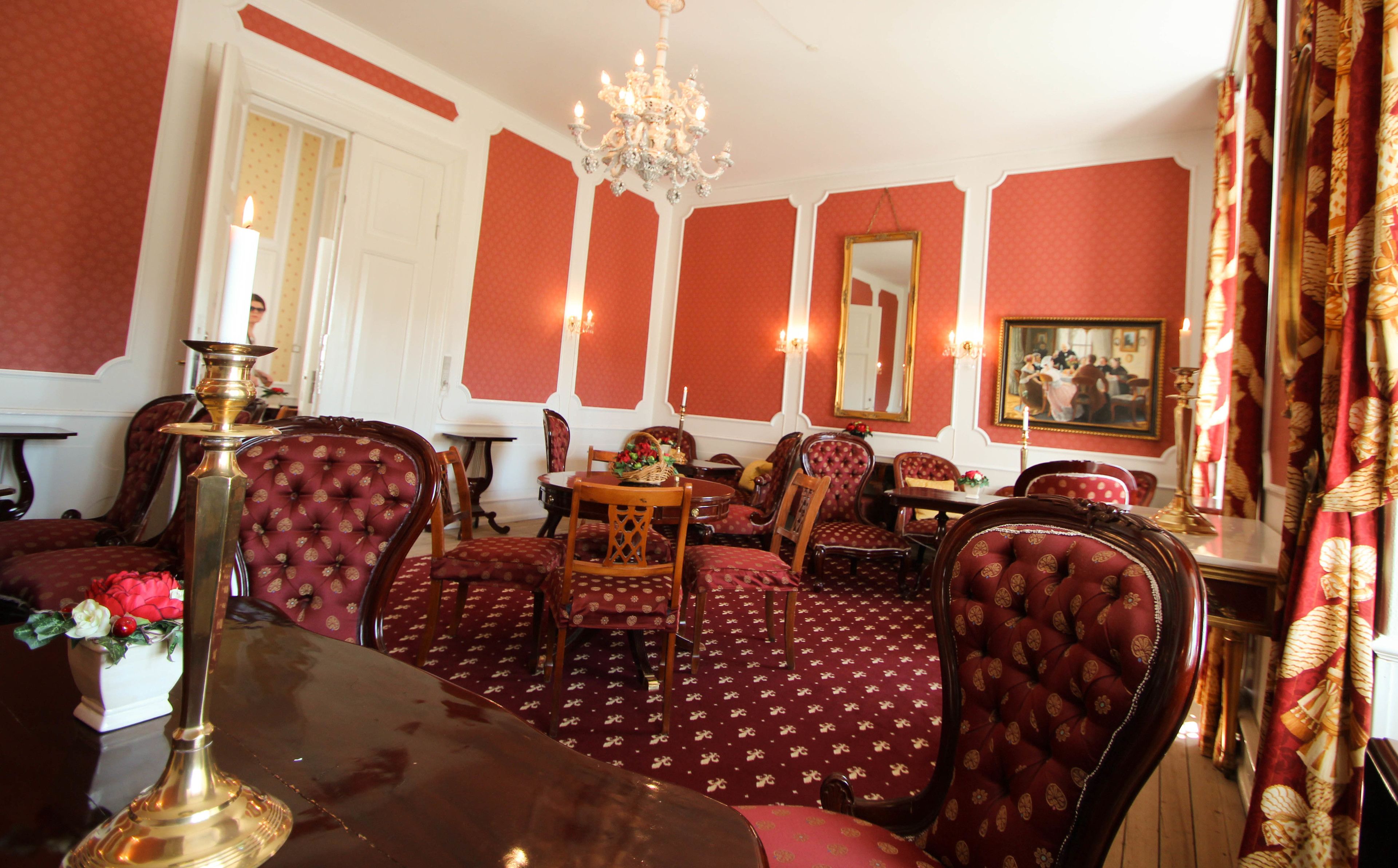 A dining room with red patterned upholstery, a chandelier, and a table with a candle holder.