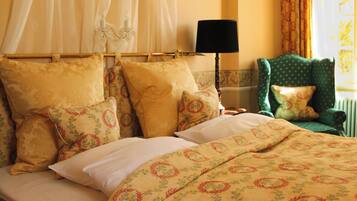 Una cama con ropa de cama y almohadas estampadas con motivos florales, una lámpara de noche y una silla con cojín.