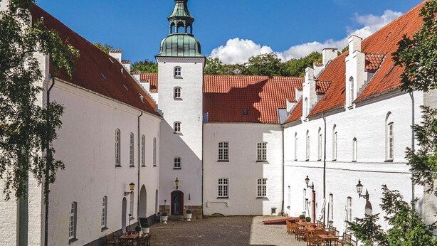 A courtyard with white buildings, a tower with a green dome, and outdoor seating.