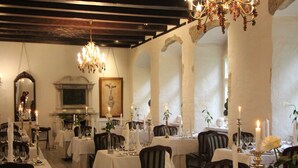 A dining area with tables set for a meal, chandeliers, and a fireplace.