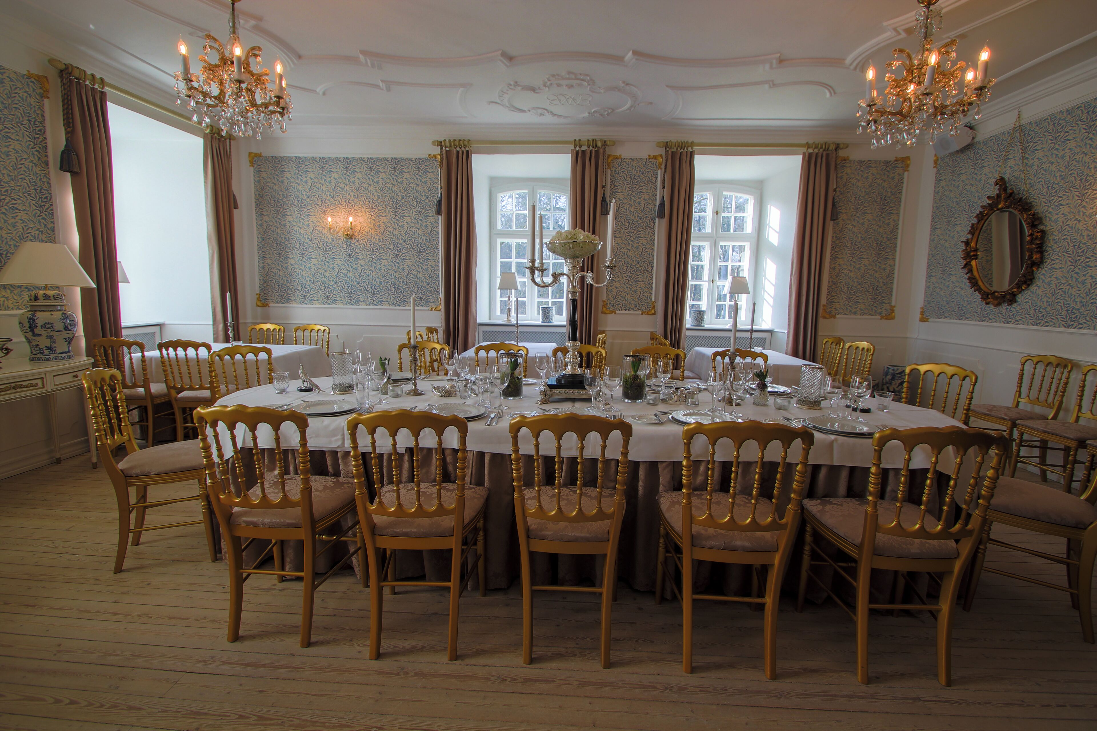Ein formeller Speisesaal mit einem runden Tisch, gedeckt für eine Mahlzeit, umgeben von Holzkreisl mit gepolsterten Sitzflächen.