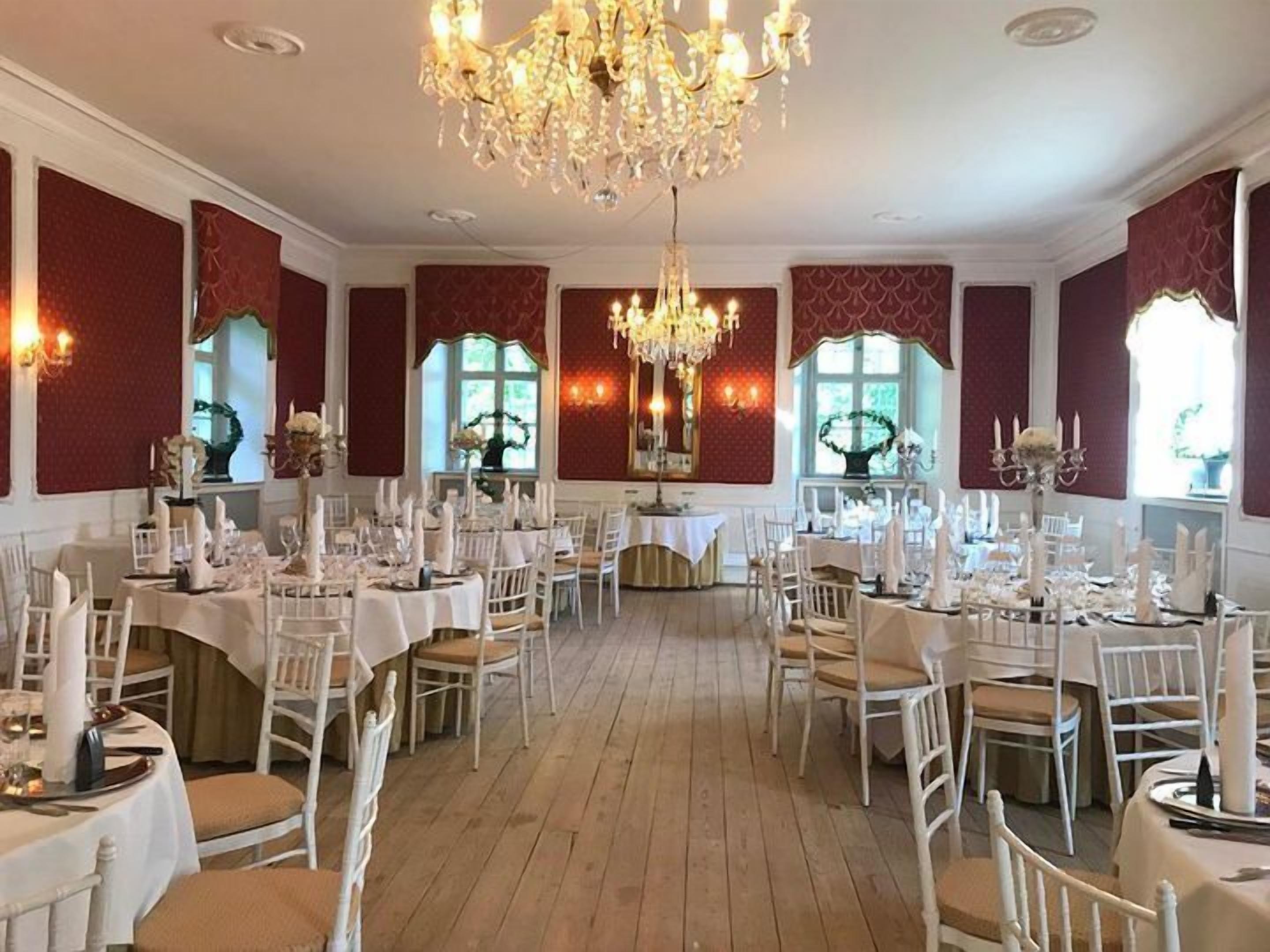 Ein formeller Speisesaal mit mehreren gedeckten Tischen, eleganten Kronleuchtern und großen Fenstern mit Vorhängen.