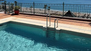 A pool with clear blue water, a metal fence, and a view of the beach and ocean.