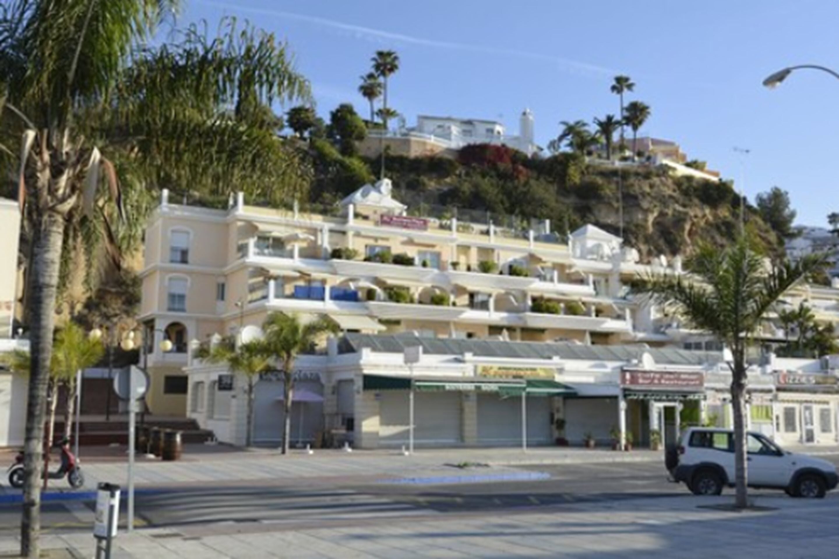 Un edificio costero con varios balcones, una calle empedrada y palmeras.