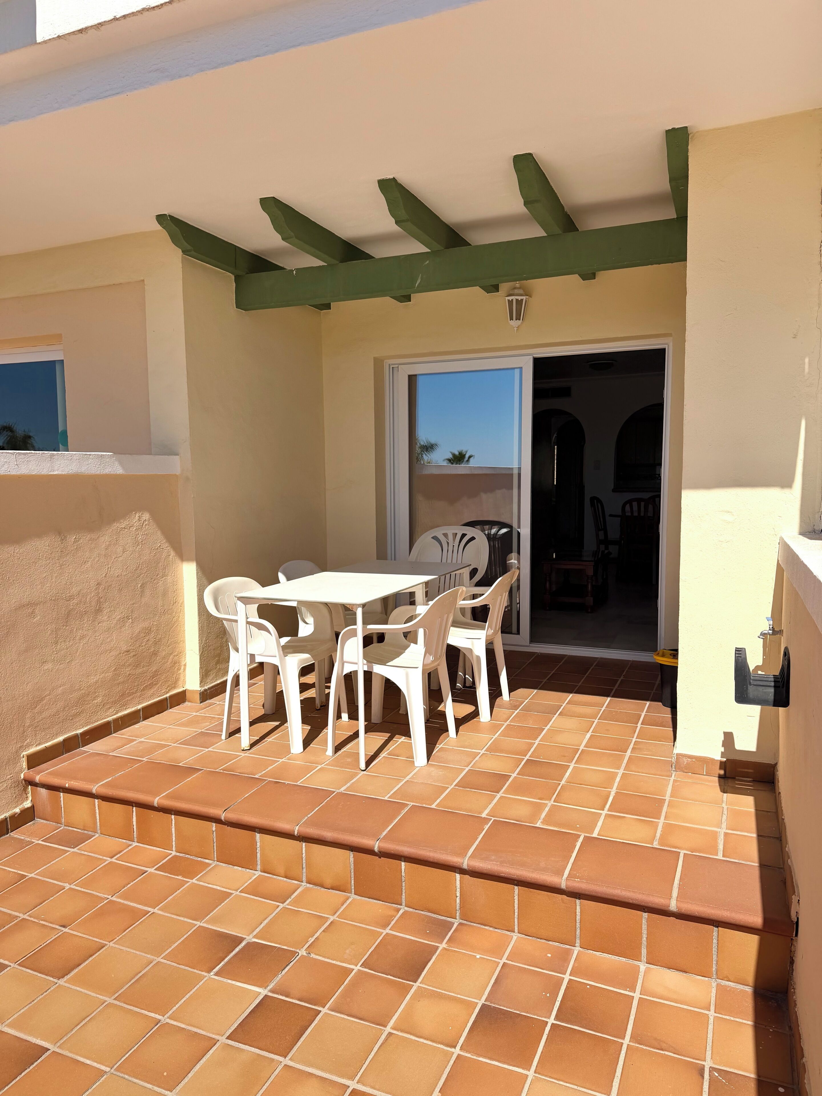 Une terrasse avec une table et des chaises, un sol carrelé et une porte donnant sur un espace intérieur.