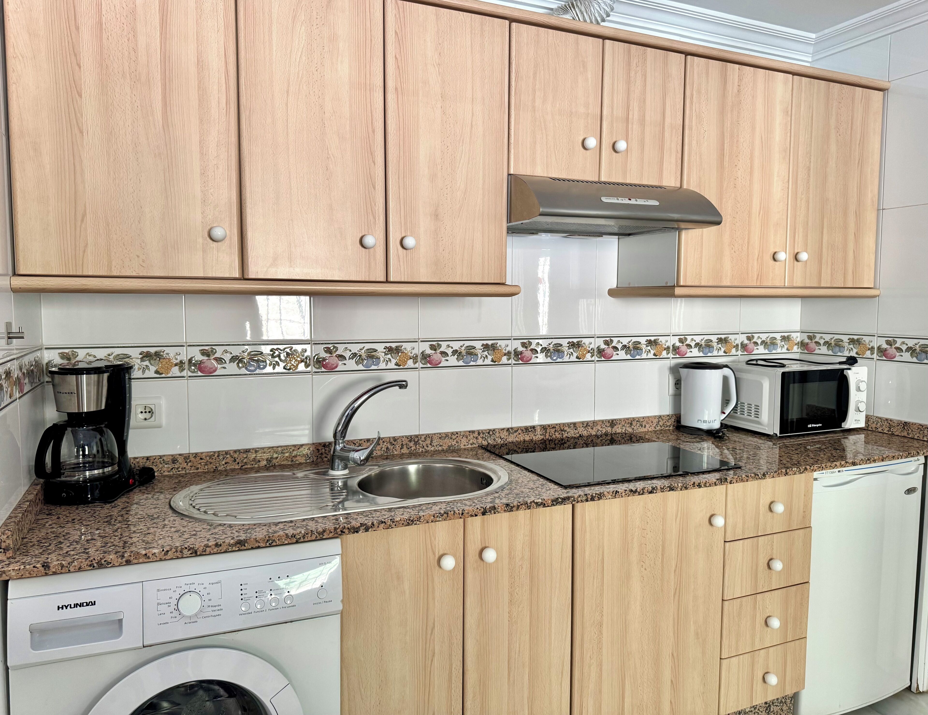 A kitchen with wooden cabinets, a stainless steel sink, a microwave, a coffee maker, and a washing machine.