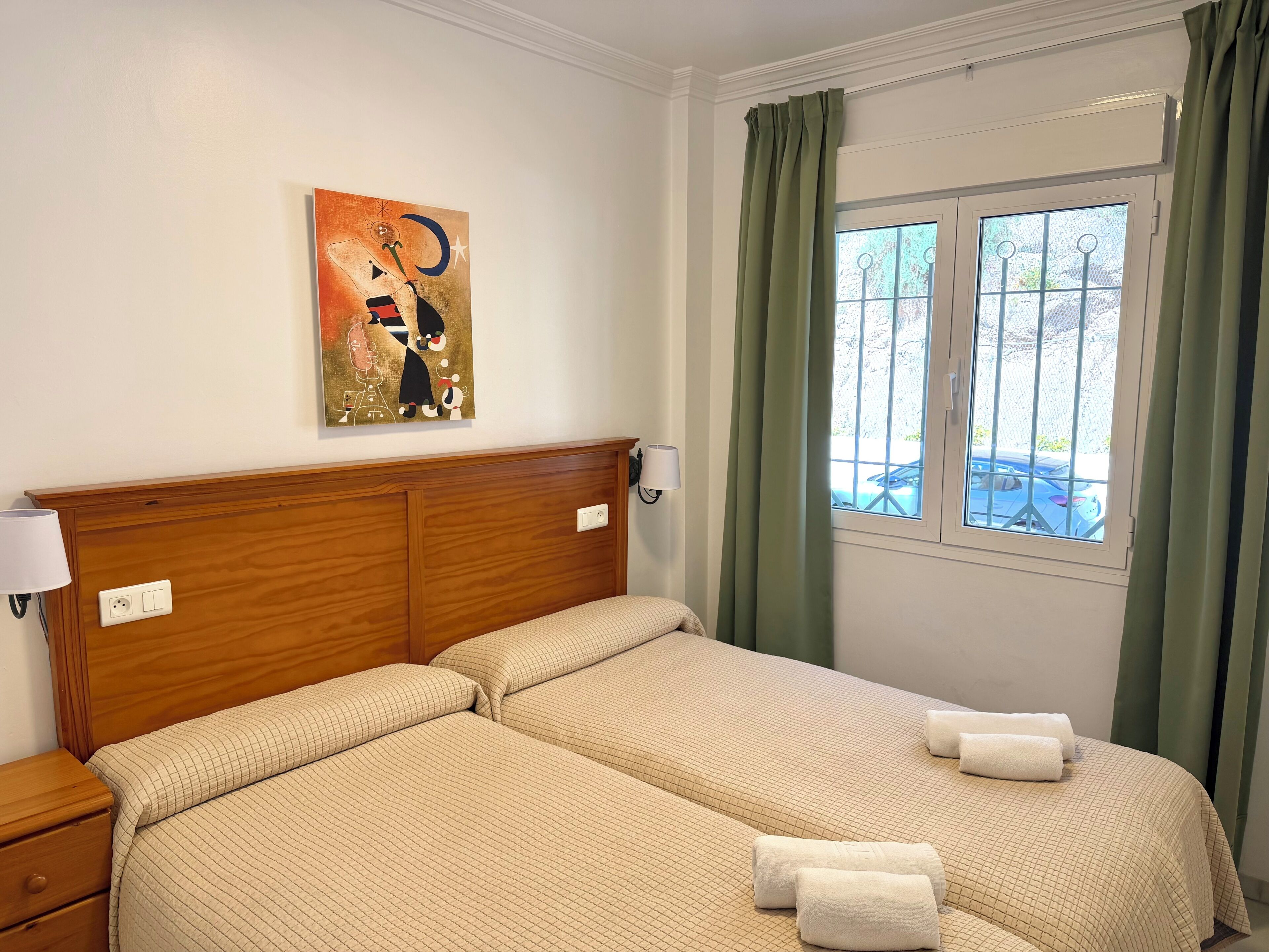 Une chambre d’hôtel avec une tête de lit en bois, un tableau au mur, une fenêtre avec des rideaux et un lit avec des serviettes.