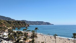 A beach with palm trees, a clear sky, and a mountainous backdrop.