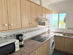 Una cocina con armarios de madera, horno integrado, microondas, cafetera, lavamanos y ventana con vistas.