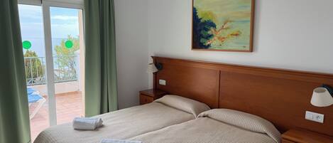A hotel room with a bed, a nightstand, a painting, and a view of the sea through a sliding door.
