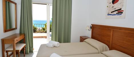 Habitación de hotel con cama, escritorio, silla y vista al mar por la ventana.