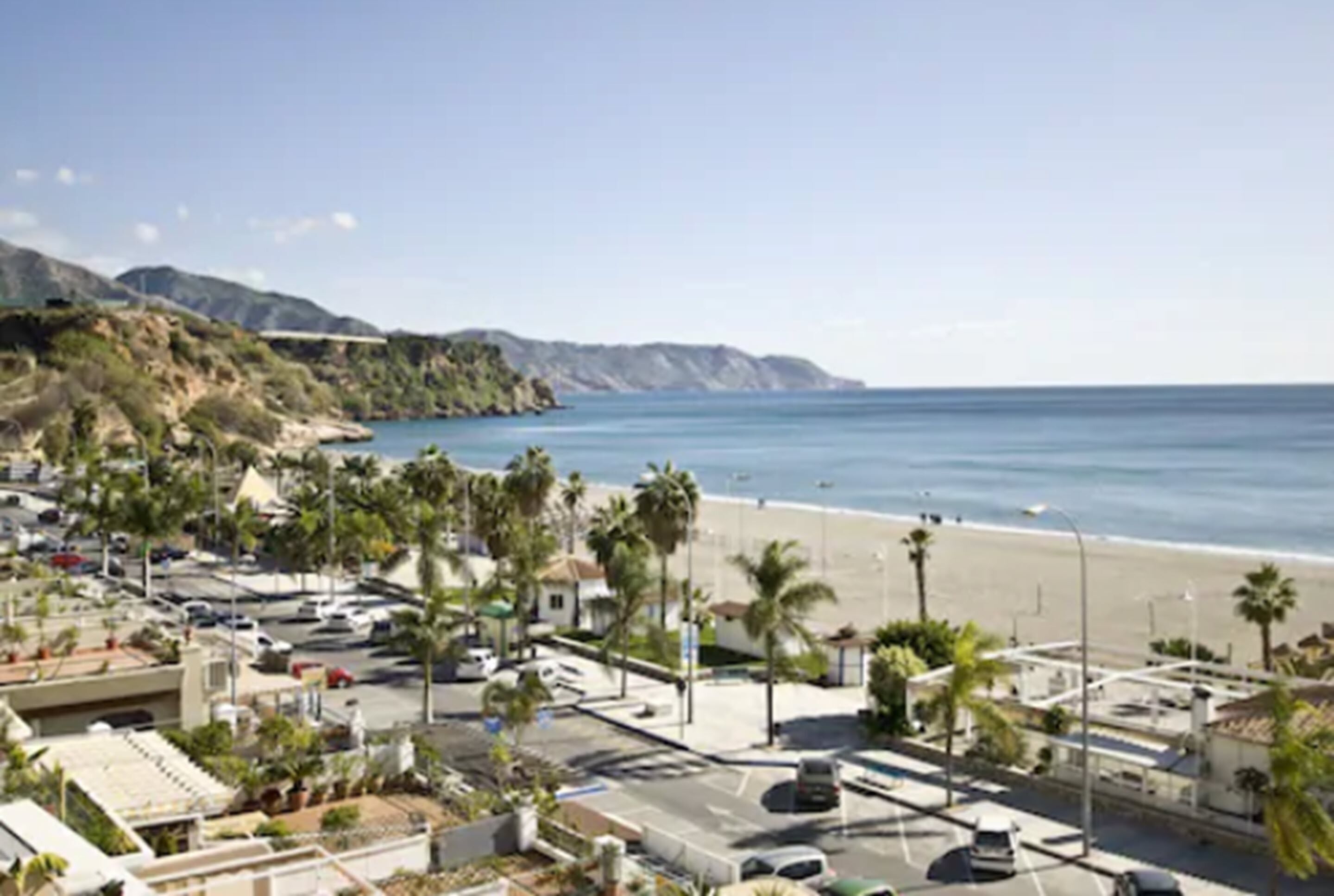 A coastal town with a beach, palm trees, and a road leading to the beach.