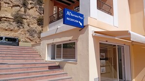A hotel entrance with a reception sign, a staircase leading up, and a vehicle parked nearby.
