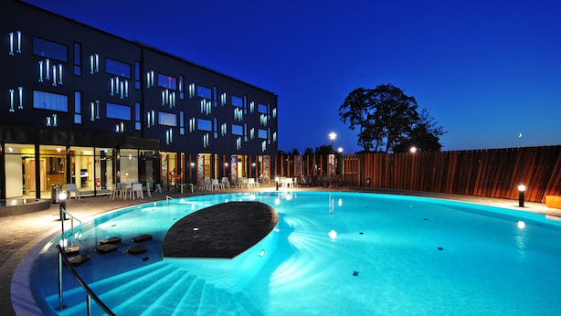 Una piscina con un edificio moderno al fondo, rodeada por una valla de madera.