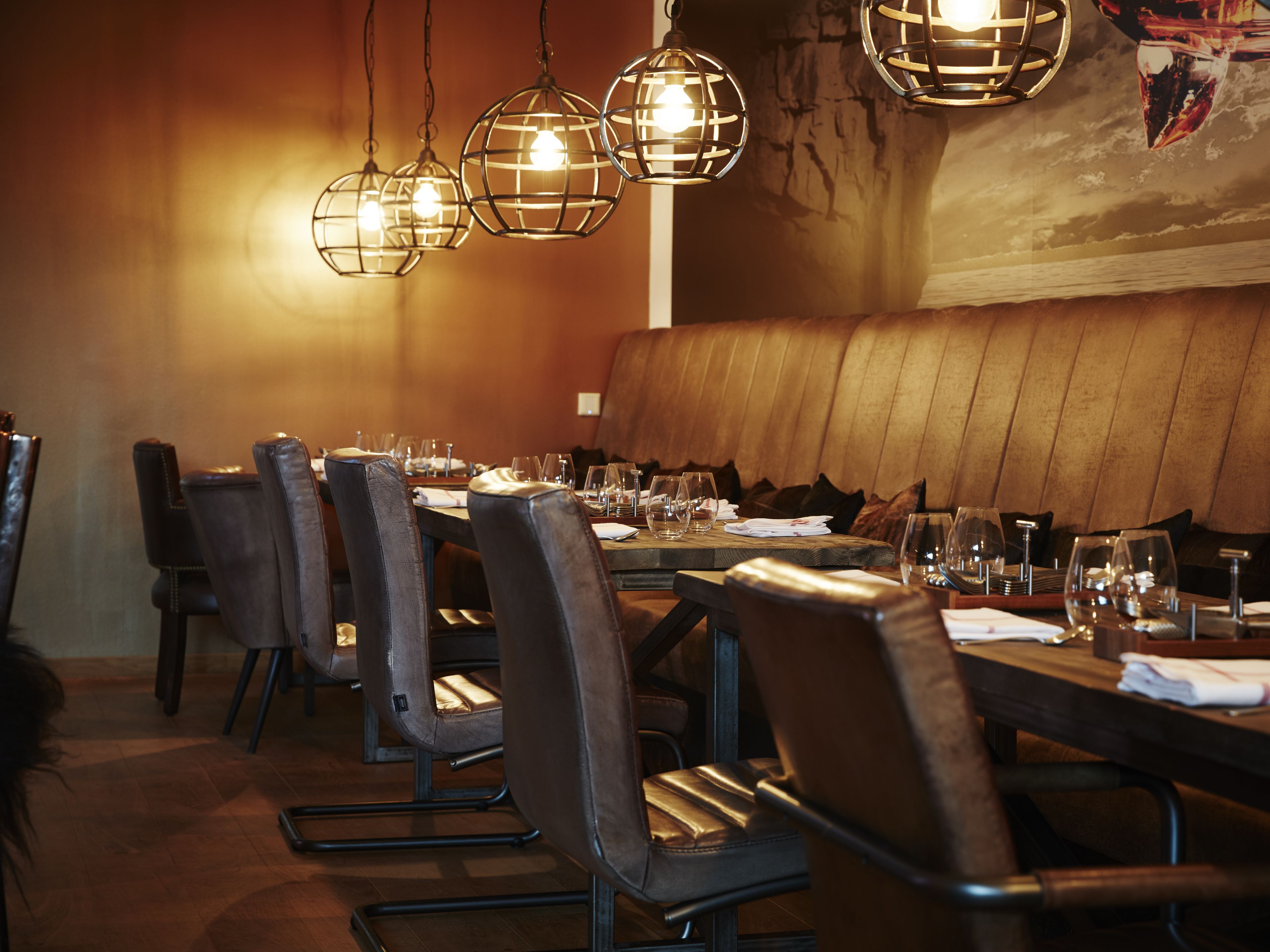 En restaurant med et langt træbord, læderstole og hængende pendellamper.