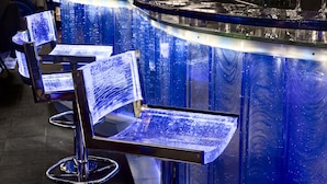 Una zona de bar con barra curva y paneles de vidrio azul iluminados.