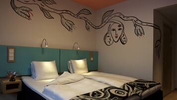 A bedroom with a bed, two bedside lamps, a wall mural, and a nightstand with a glass bowl.