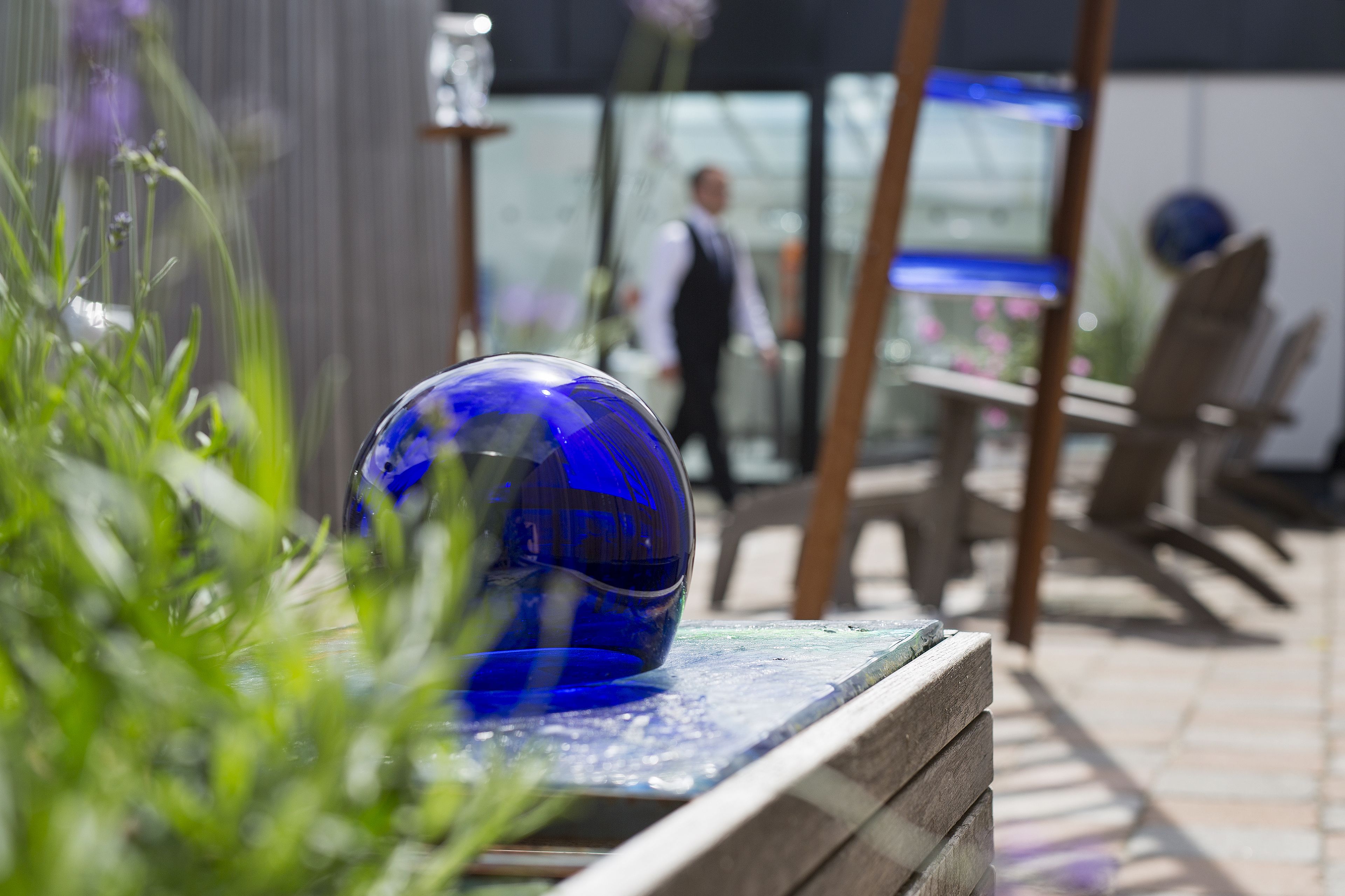 A blue glass sculpture on a wooden bench in an outdoor setting with chairs and tables in the background.