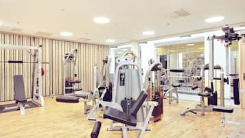 A gym with various exercise machines, wooden floors, and large windows.