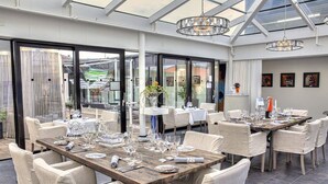 Un restaurante con varias mesas dispuestas para comer, amplios ventanales y una moderna lámpara de araña.