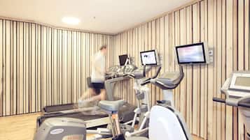 Ein Fitnessraum mit Trainingsgeräten, Holzwandverkleidung und einem Fernsehbildschirm.