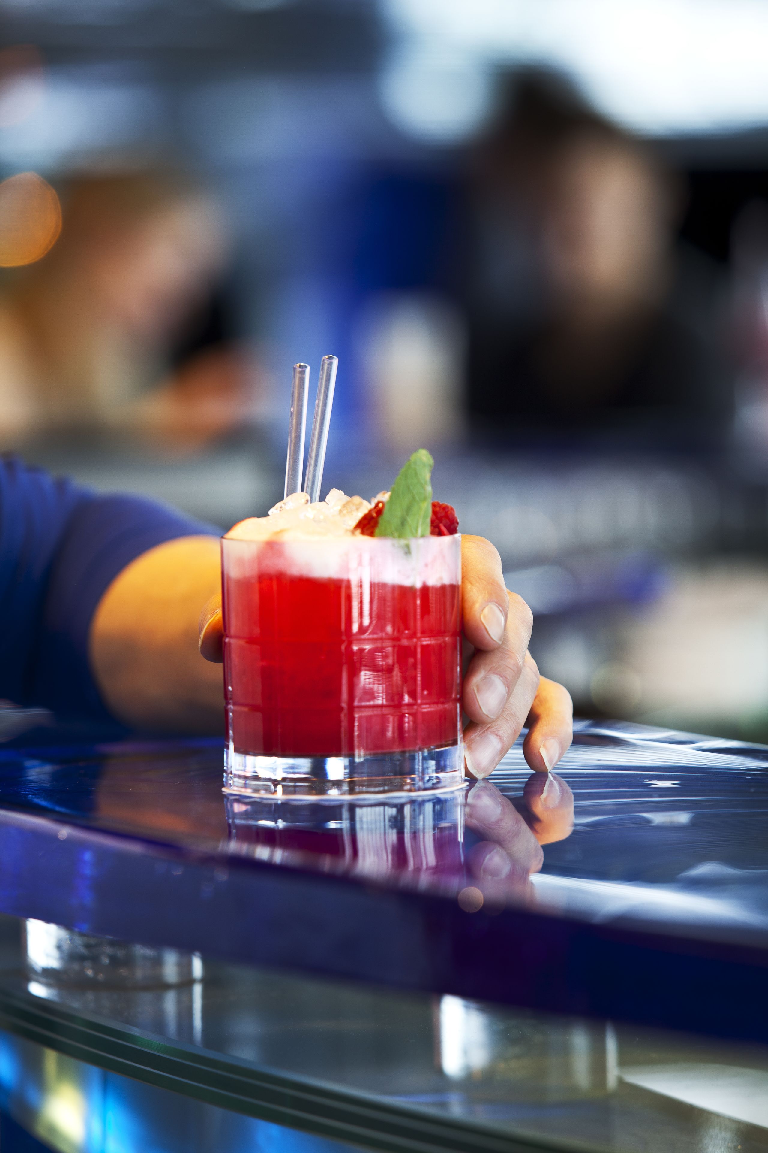 Een hand die een cocktail vasthoudt met rode vloeistof, ijs en een muntblaadje.