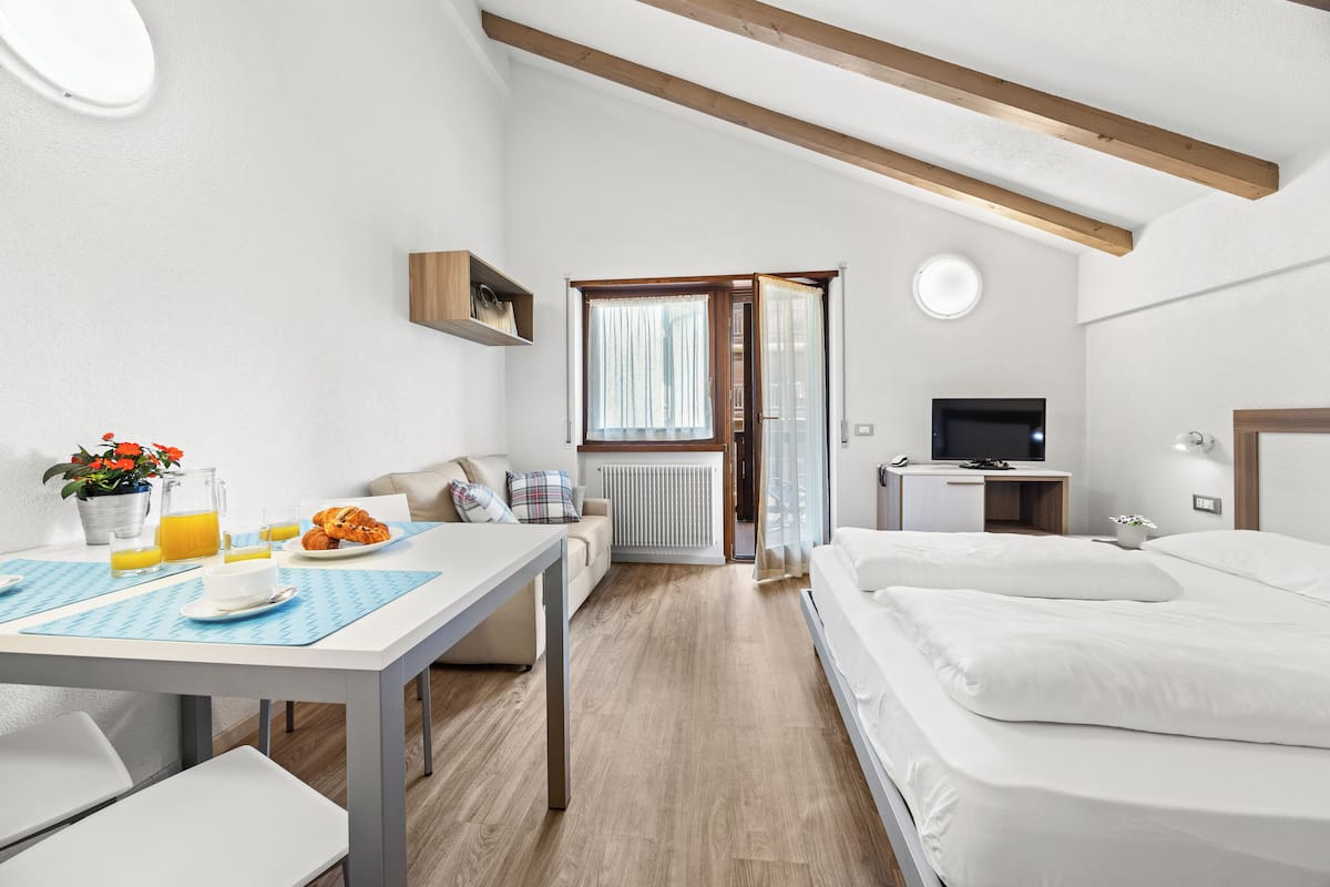 A modern hotel room with a wooden ceiling, a dining area with breakfast, a bed, and a TV.