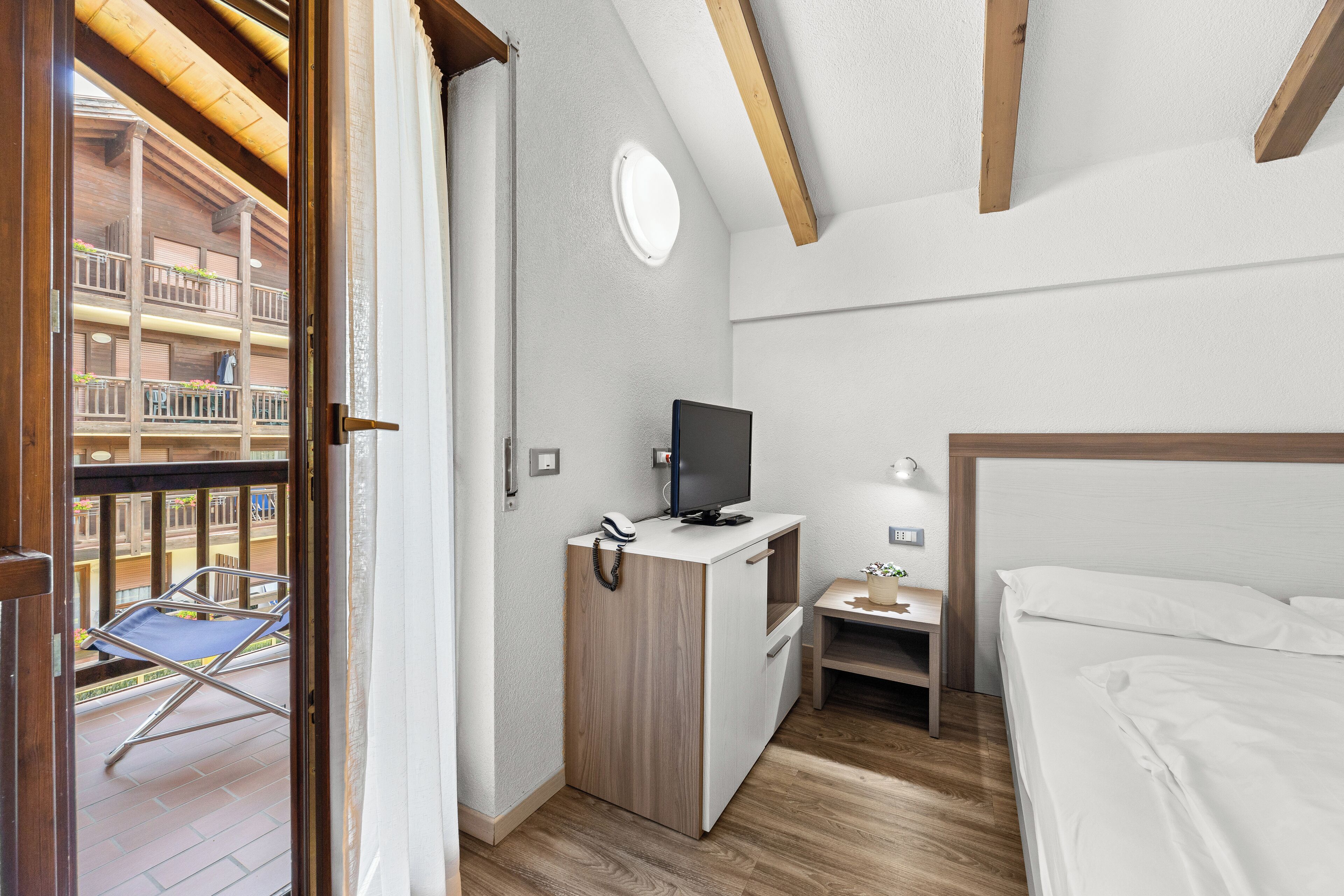 Habitación de hotel con cama, escritorio con televisor, una mesita y balcón con silla.