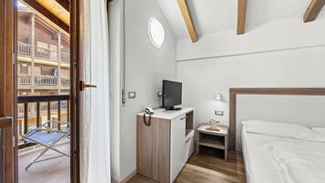 Habitación de hotel con cama, escritorio con televisor, una mesita y balcón con silla.