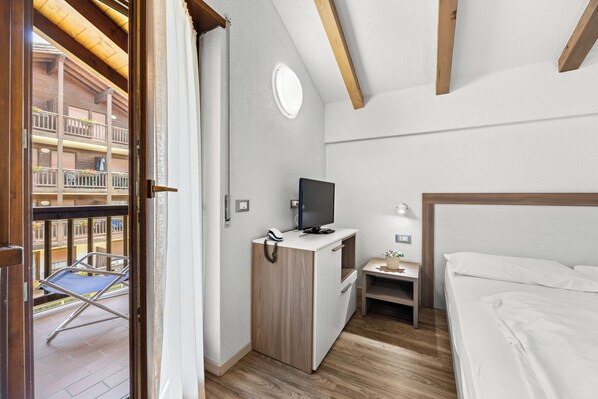 Habitación de hotel con cama, escritorio con televisor, una mesita y balcón con silla.