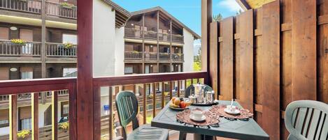 Un balcon avec une table dressée pour deux personnes, donnant sur un immeuble doté de nombreux balcons.