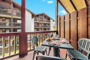 A balcony with a table set for two, overlooking a building with multiple balconies. - Aparthotel Des Alpes (Cavalese)
