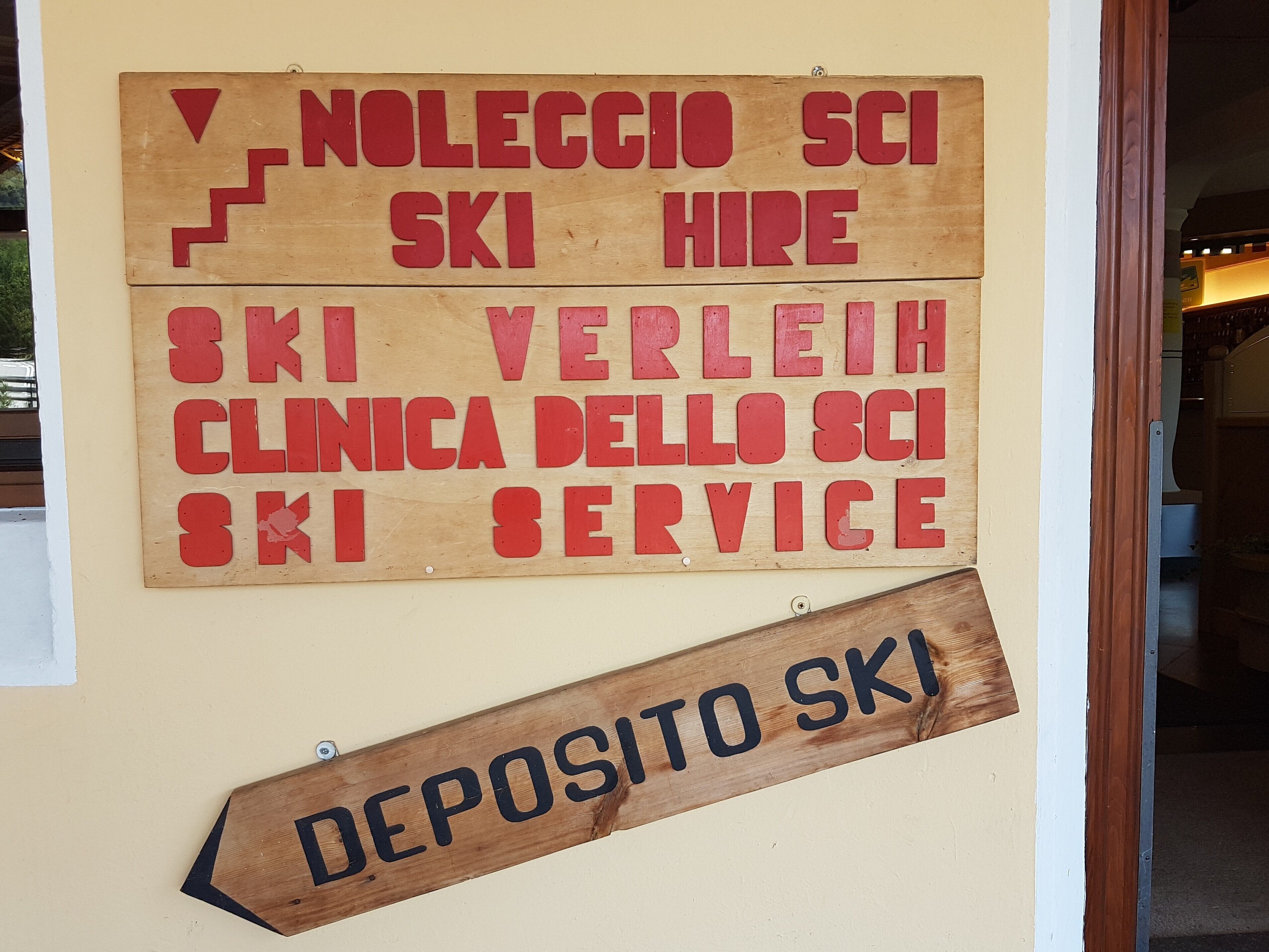 Une enseigne en bois avec une inscription rouge faisant la publicité de services liés au ski et indiquant la présence d’une boîte de dépôt.